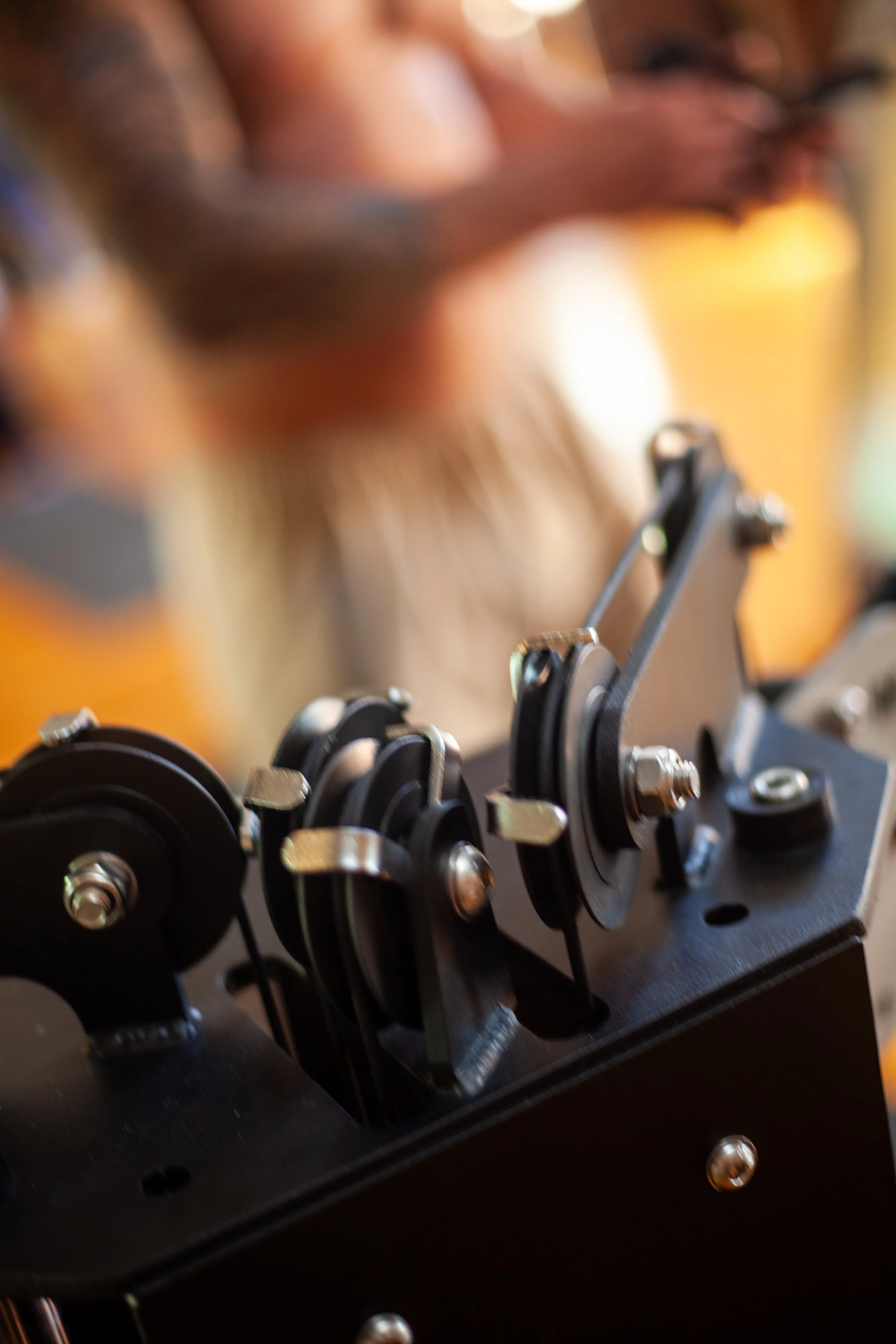 Close-up of a mechanical device with gears and pulleys, with a person operating it in the background, blurred.