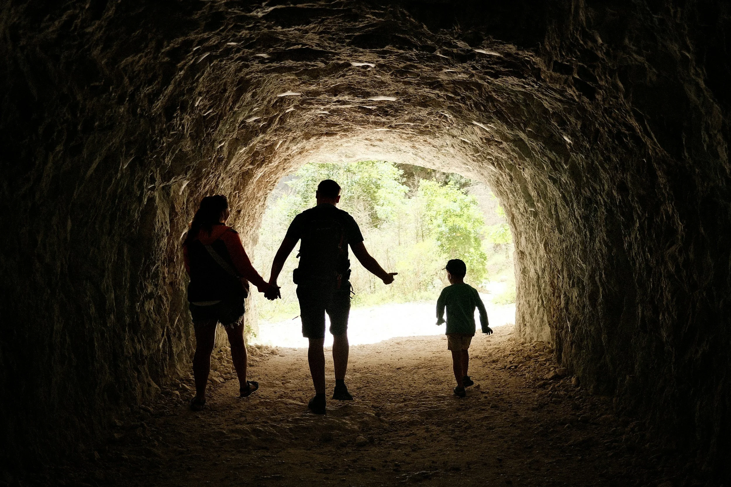 Adults and a child walking through a rocky tunnel into daylight, representing family support and guided pathways in Bourne.