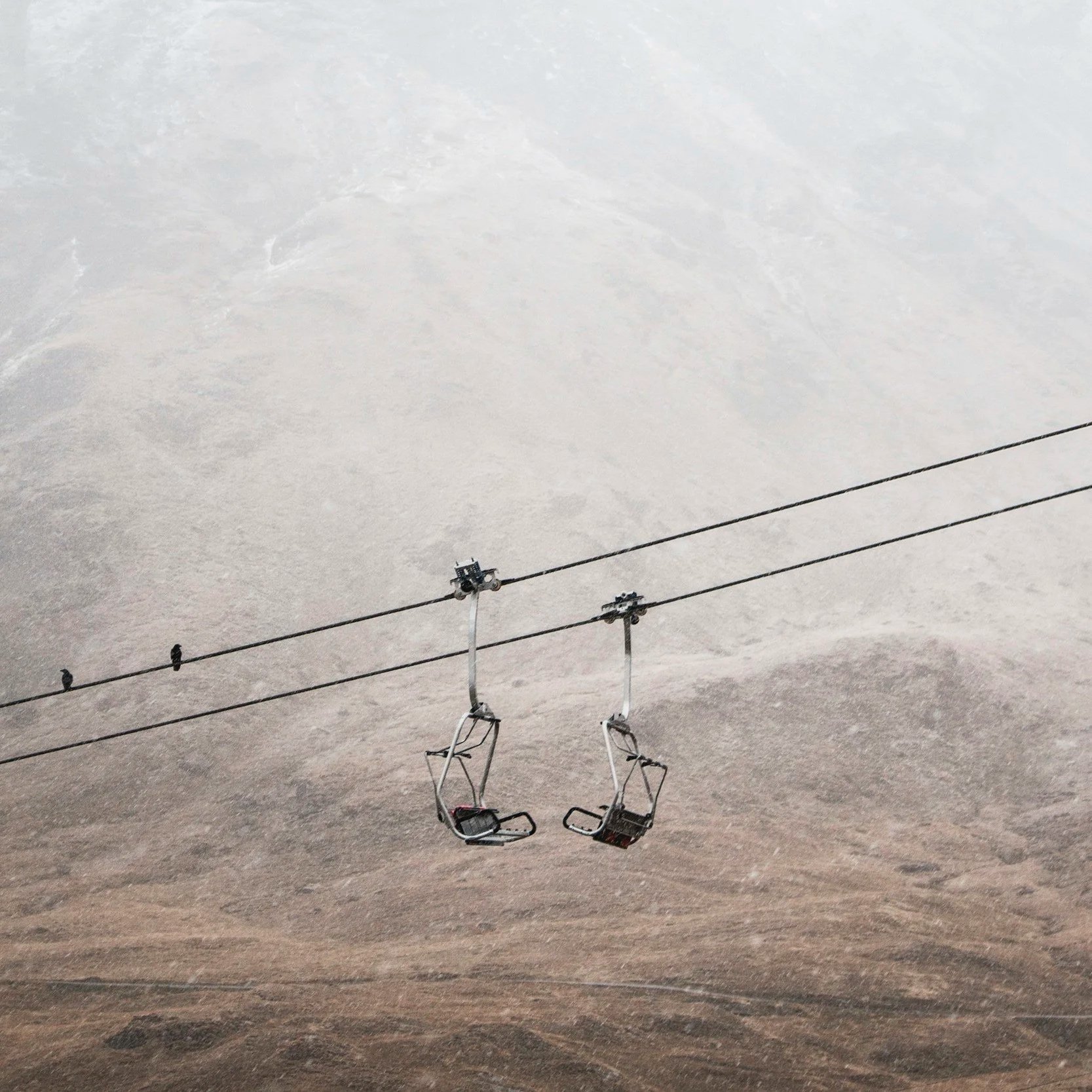 Deux chaises de téléphérique suspendues dans un paysage aride et montagneux avec un ciel nuageux.