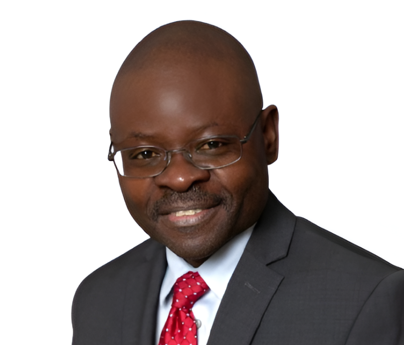 A professional bald African American man wearing glasses, a dark suit, white shirt, and red tie, smiling at the camera against a white background.