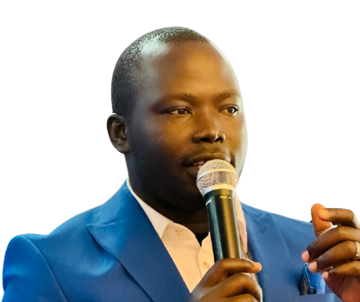 A man speaking into a microphone, wearing a blue suit and white shirt, with a neutral background.