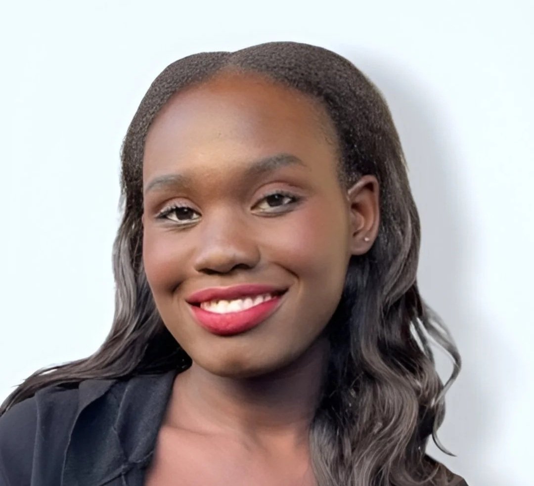 Portrait of a young African American woman with wavy hair, smiling and wearing makeup, against a light background.