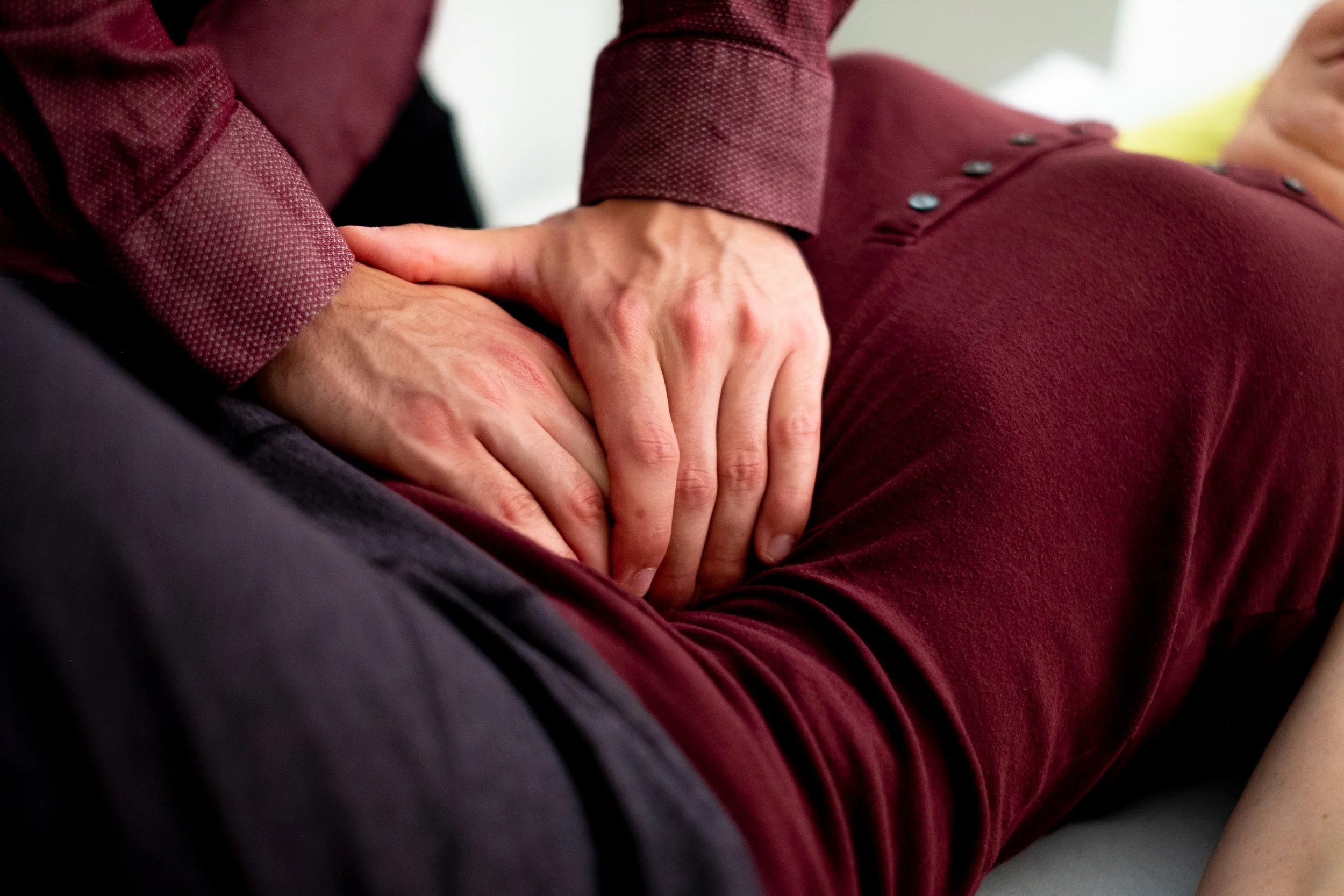 Jérémie Houle effectue une technique ostéopathique dans la région abdominale d'une autre personne allongée sur un matelas, vêtue d'un vêtement pourpre.