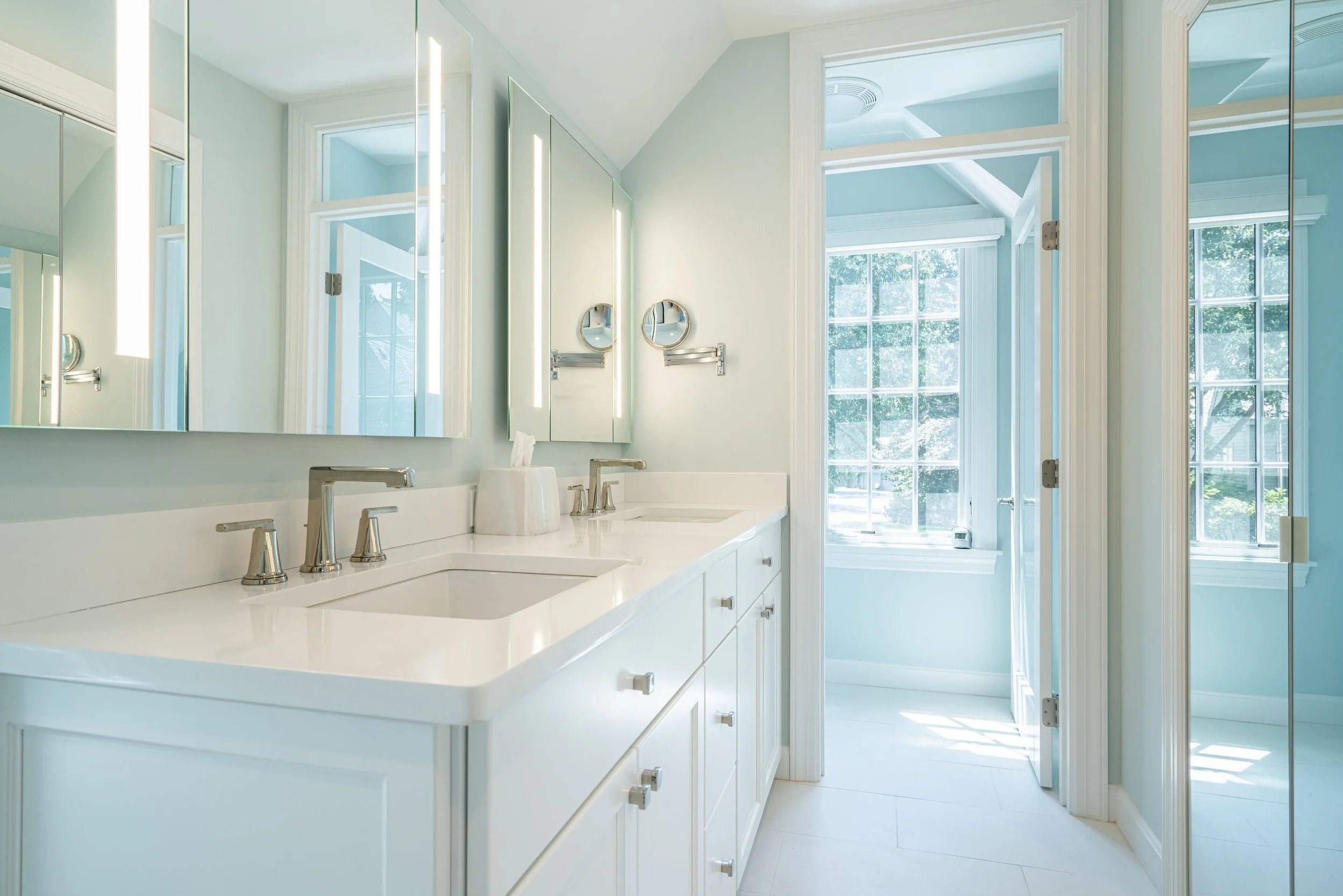 Bright bathroom with white double sink vanity, large mirror, and natural light from windows.