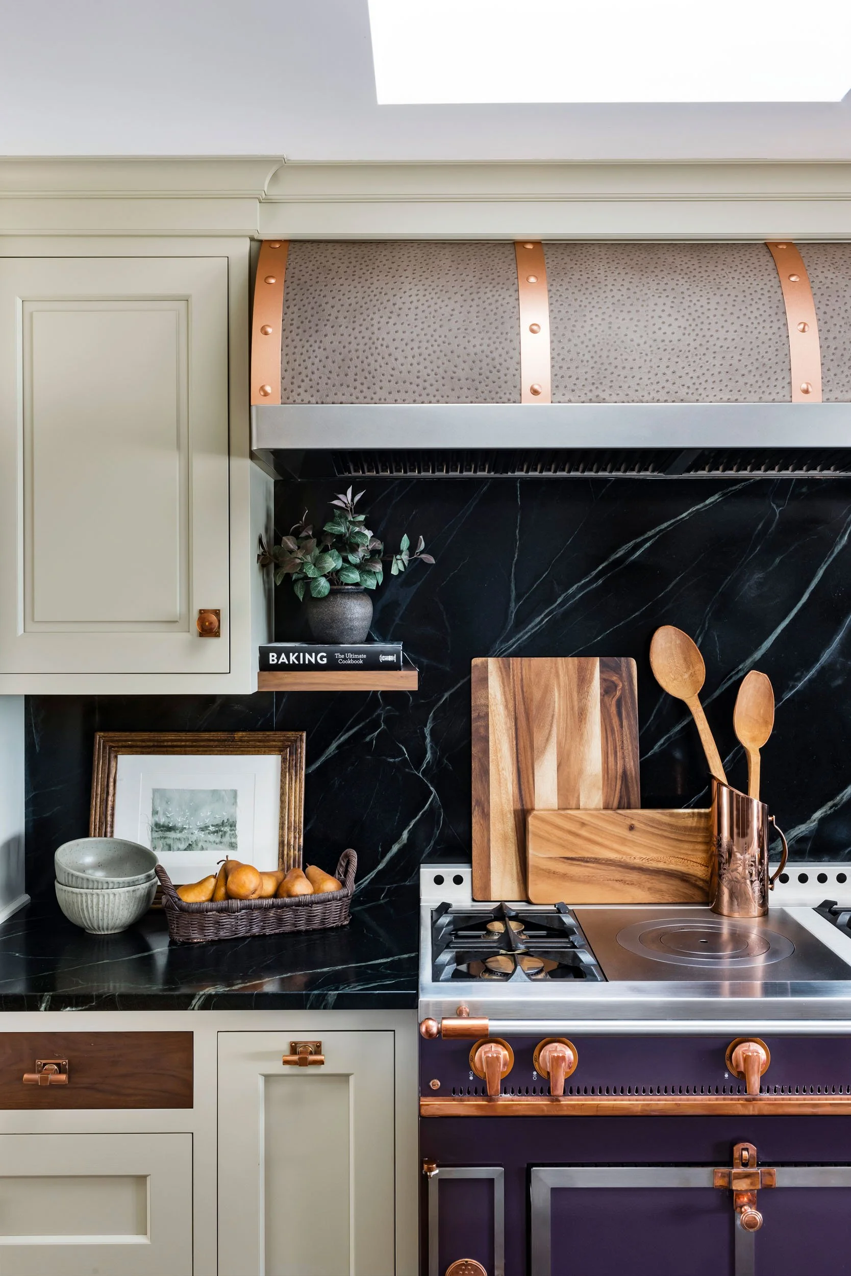 Modern kitchen with cream cabinets, black marble backsplash, copper accents, wooden utensils, and decorative items.