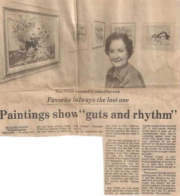 A newspaper clipping featuring a black-and-white photo of an elderly woman at an art exhibit, with framed paintings on the wall behind her. The headline reads 'Paintings show guts and rhythm,' with a quote: 'Favorite is always the last one.'