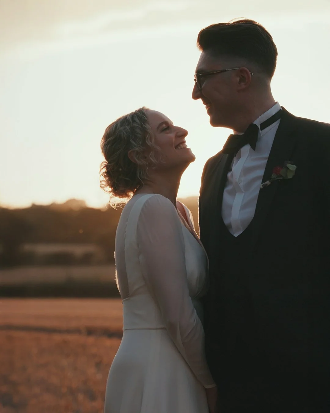 A happy couple on their wedding day smiling at each other during sunset in an outdoor setting.