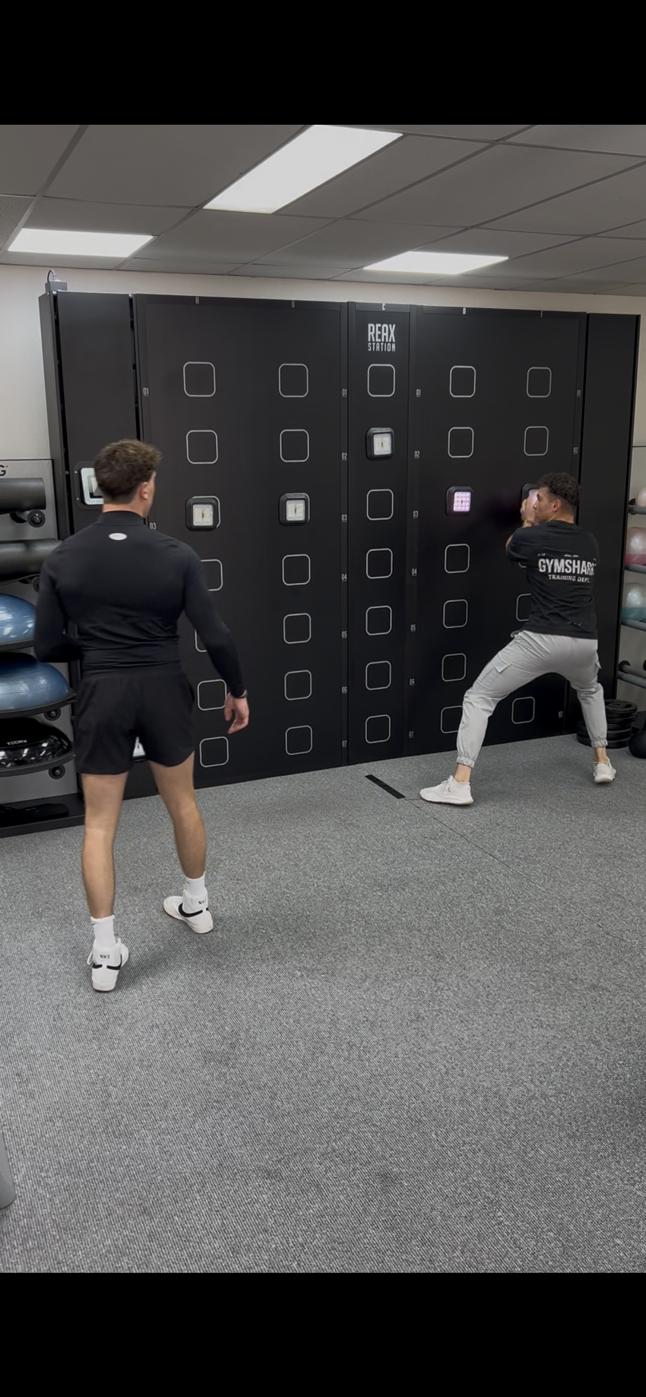 Twee mannen trainen in een sportschool met een groots beveiligingskast met schuifdeuren en digitale sloten.