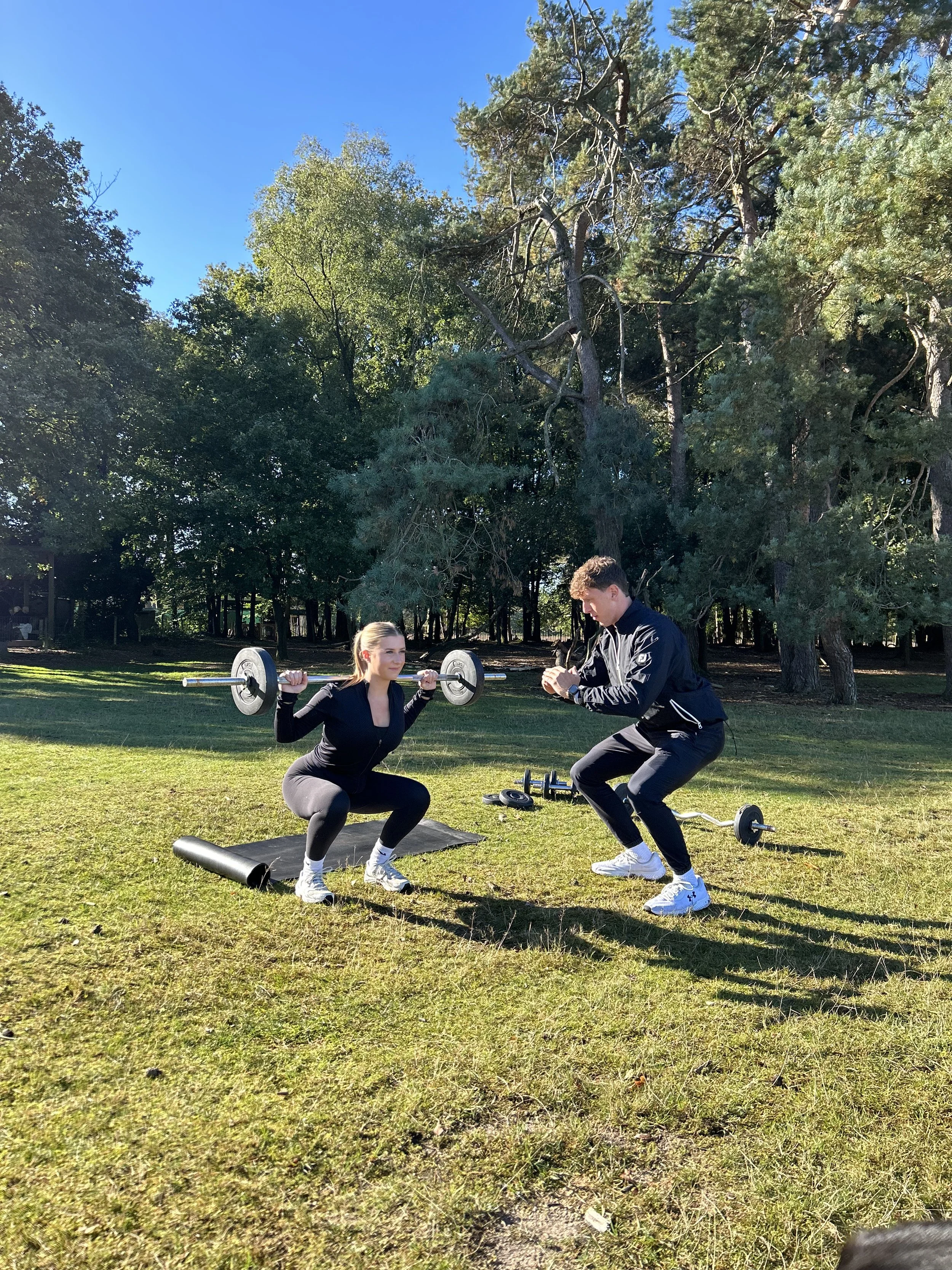 Vrouw doet squats met halters onder toezicht van een man in een park.