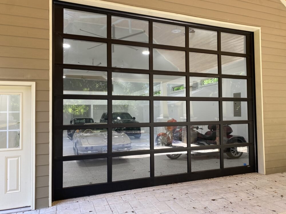Large black-framed glass garage door showing cars and motorcycles inside and outside the garage.