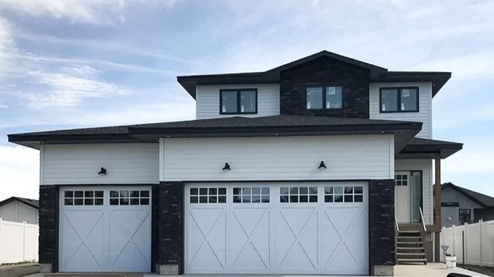 New two-story house with white exterior, black stone accents, three attached garage doors, and a small front porch with stairs.