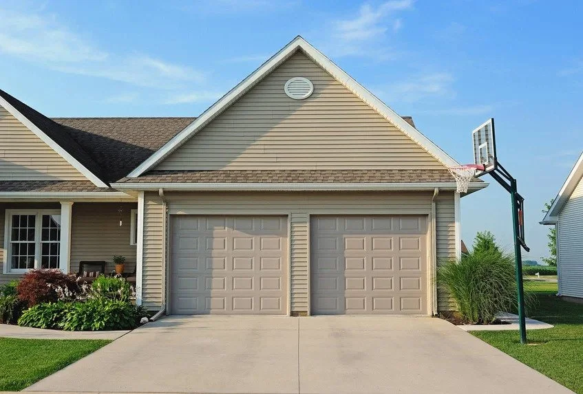A house with beige siding, a two-car garage, and a basketball hoop on a concrete driveway.