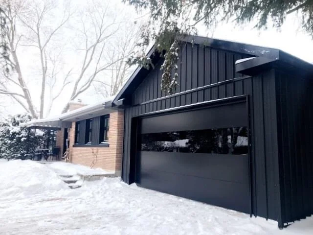 A house with brick and black siding exterior, a garage door, and a snow-covered yard.