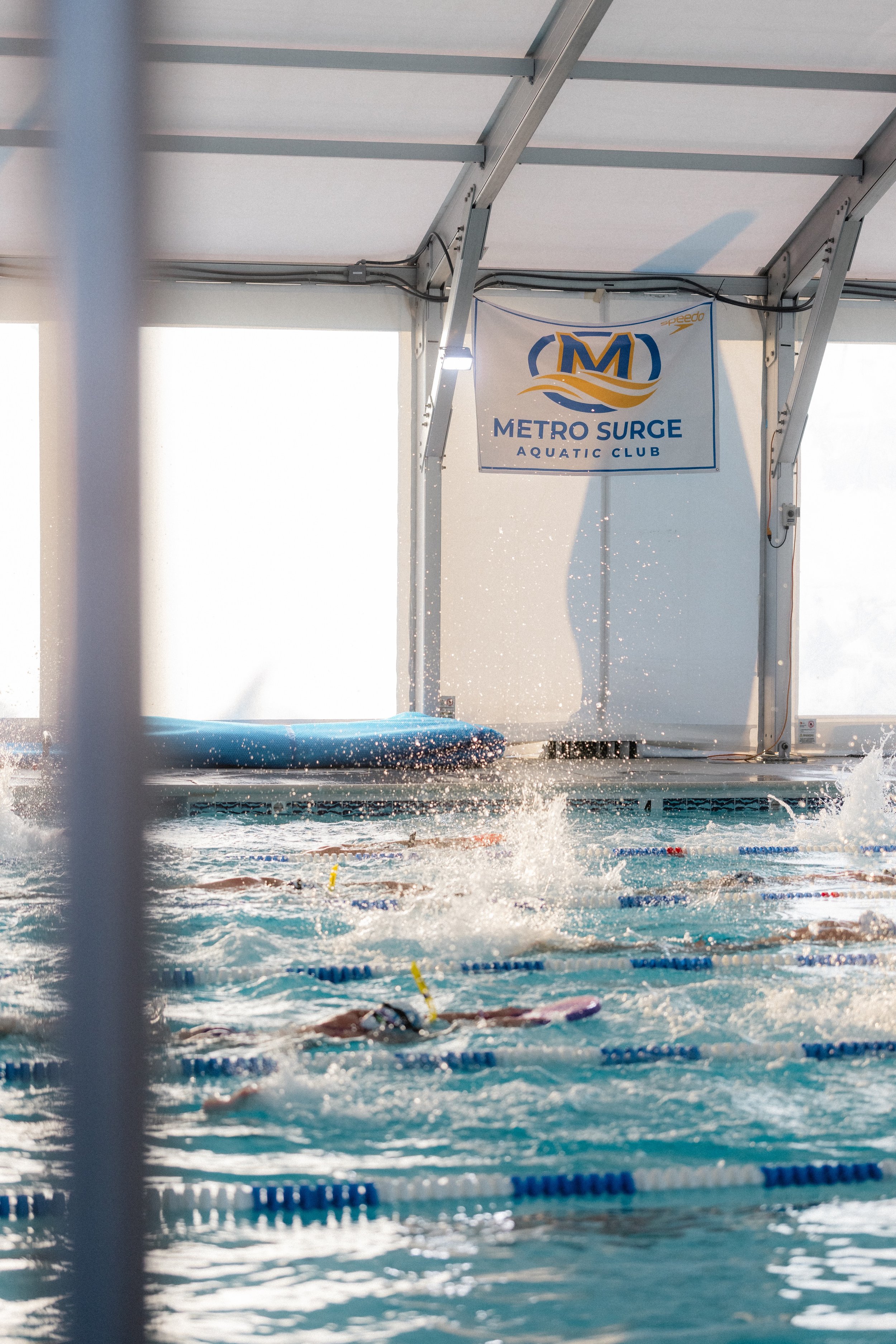 Swimmers in a swimming pool practicing at Metro Surge Aquatic Club with a banner hanging on the wall.