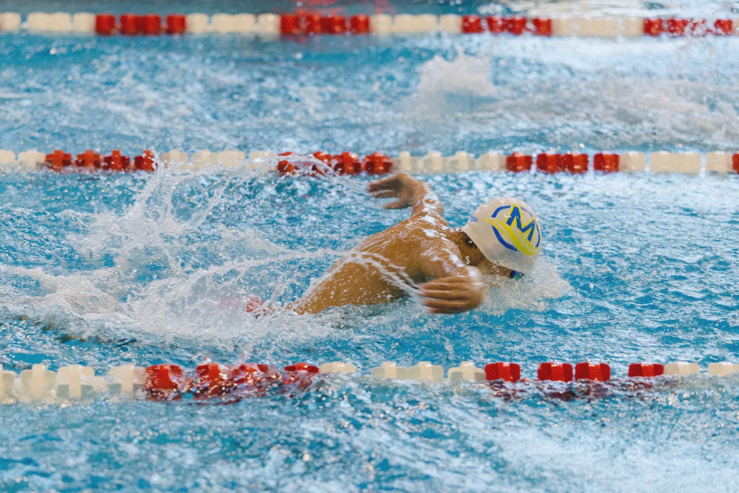 Swimmer in cap performing a butterfly stroke in a swimming pool during a race.