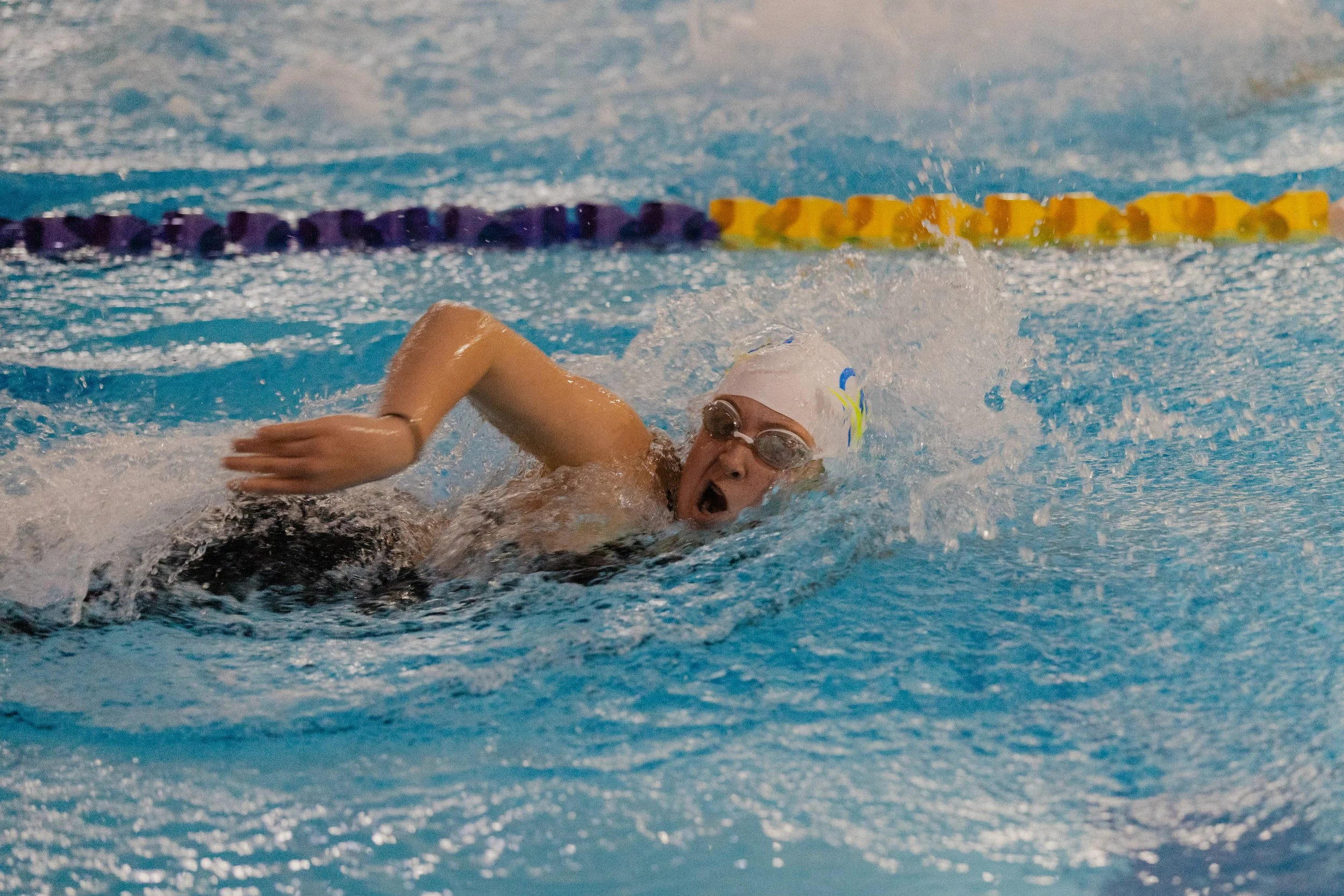 Swimmer in a swimming pool performing the front crawl stroke, wearing goggles and a swim cap.