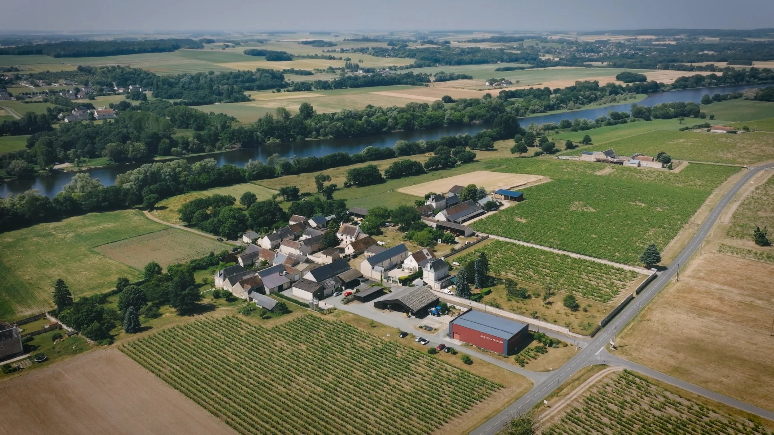 Aerial view of a rural landscape featuring a small village surrounded by farmland, vineyards, and a river.