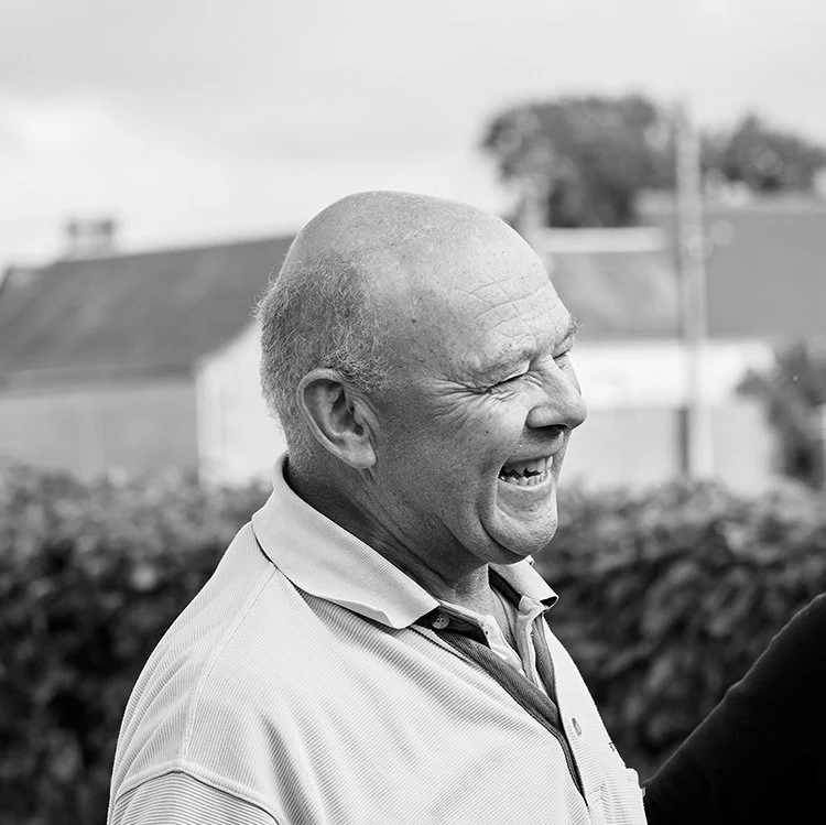 A black and white photo of a bald man smiling and laughing outdoors.