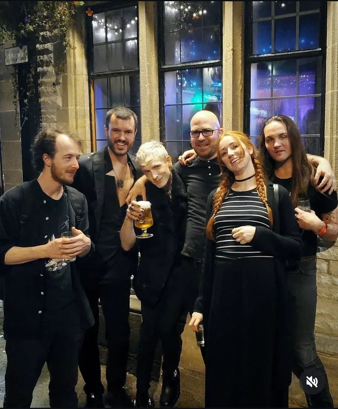 Shea Bilé and friends at a pub in Weymouth, England, smiling and holding drinks, standing in front of large windows decorated with string lights and reflections of colorful lights.
