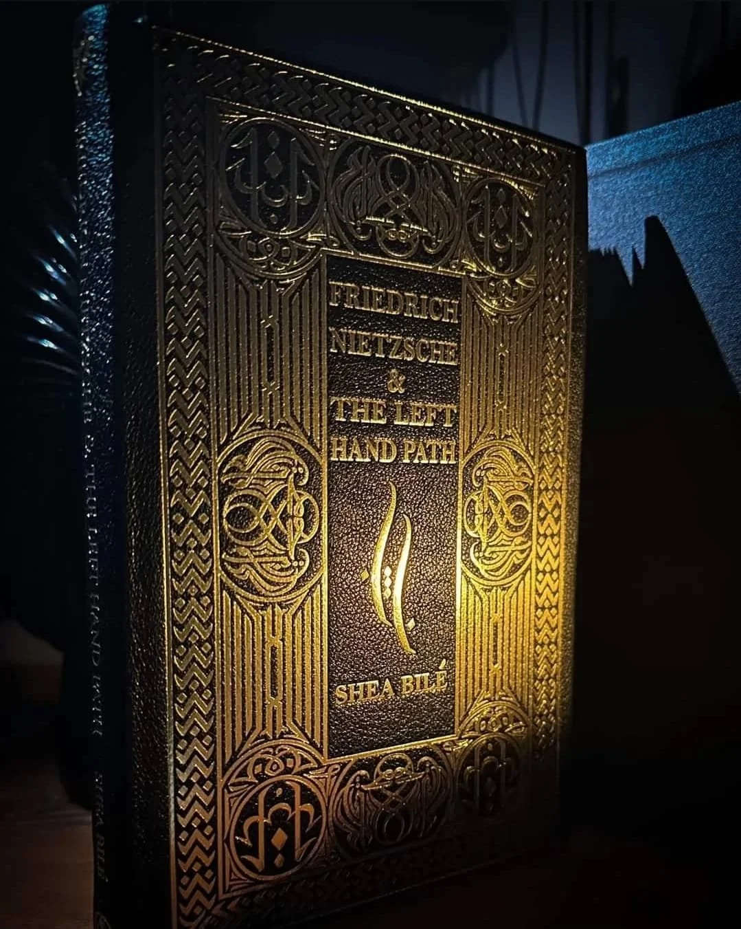 Deluxe edition book cover of Friedrich Nietzsche and the Left Hand Path by Shea Bilé (Shea Bile), featuring an ornate gold-embossed design on a black hardcover.