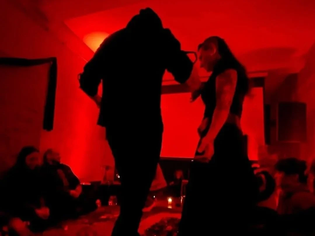 Shea Bilé participates in a glass-walking ritual in a red-lit room. Berlin, Germany.