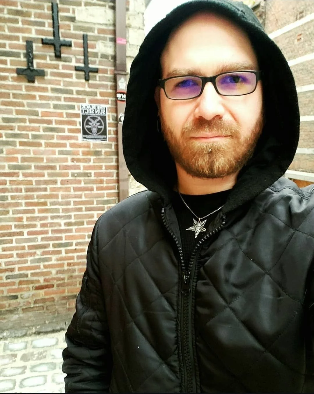 Shea Bilé taking a selfie outdoors near brick walls and inverted crosses on the wall. Leuven, Belgium.