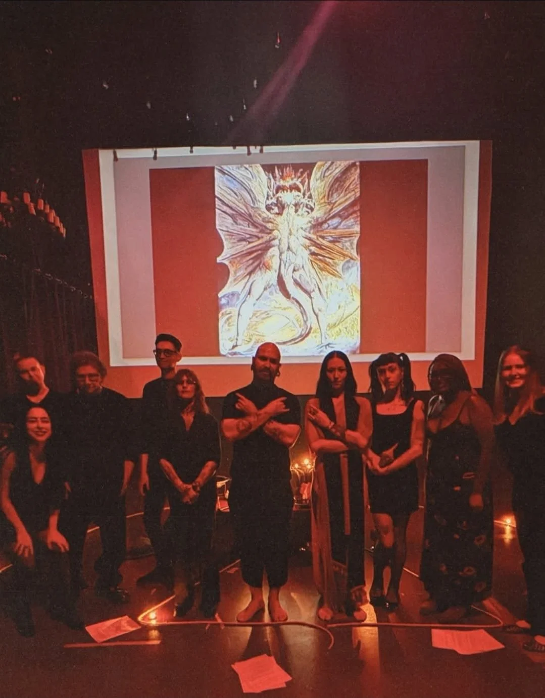 Shea Bilé and a group of people standing in front of a large screen displaying The Great Red Dragon by William Blake, in a dark room with red lighting.