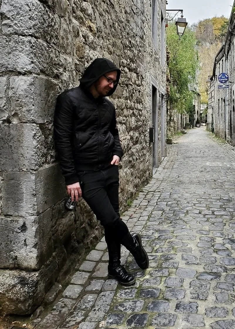 Shea Bilé leaning against a stone wall on a cobblestone street in Durbuy, Beligum. 
