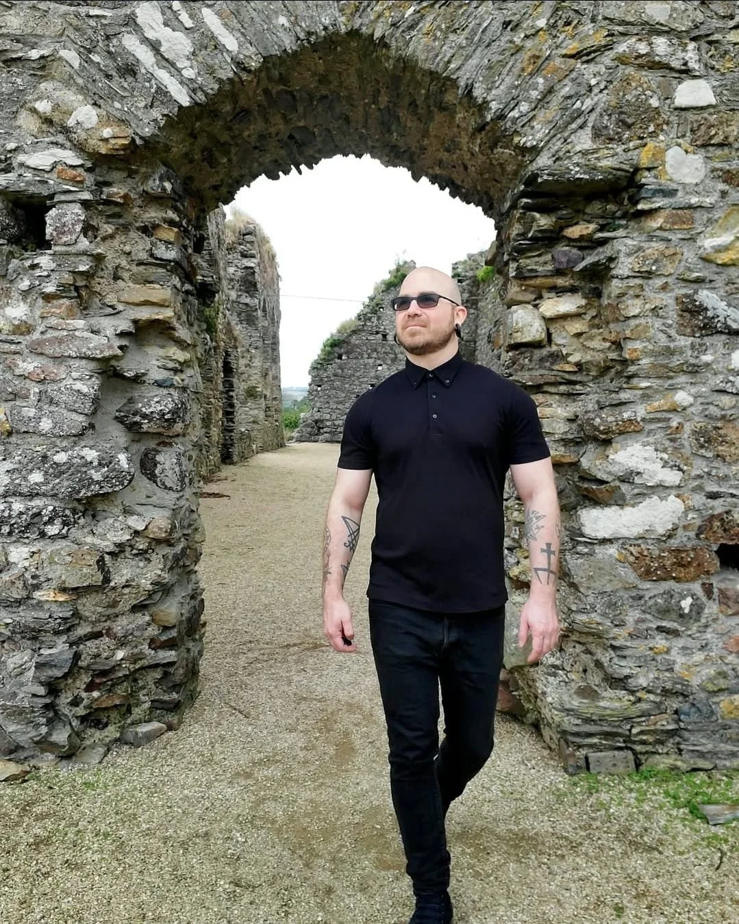 Shea Bilé wearing black clothing walking through ancient stone ruins. 