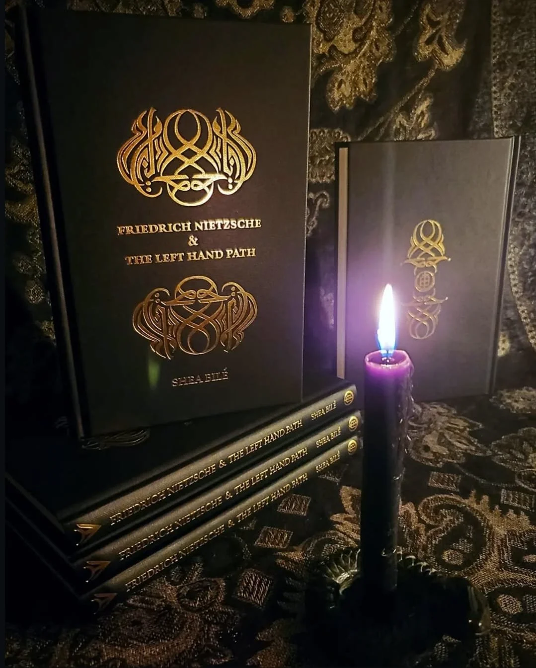 First edition hardcover copies of Friedrich Nietzsche and the Left Hand Path by Shea Bilé (Shea Bile), published by Atramentous Press, displayed beside a lit black candle in a ritual-style setting.