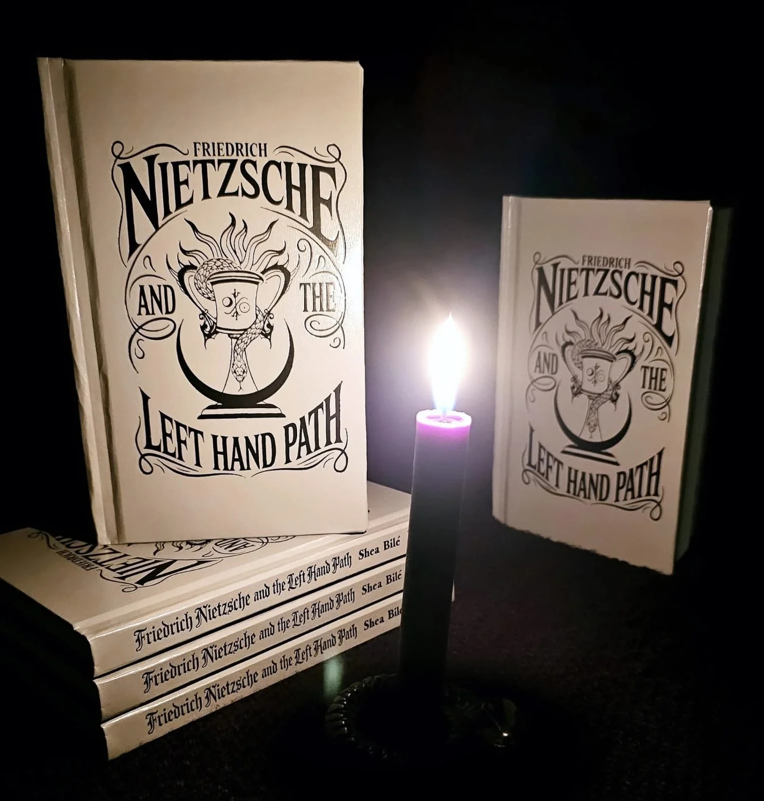 Second expanded edition hardcover copies of Friedrich Nietzsche and the Left Hand Path by Shea Bilé (Shea Bile), published by Miskatonic Books, displayed beside a lit candle against a dark background.