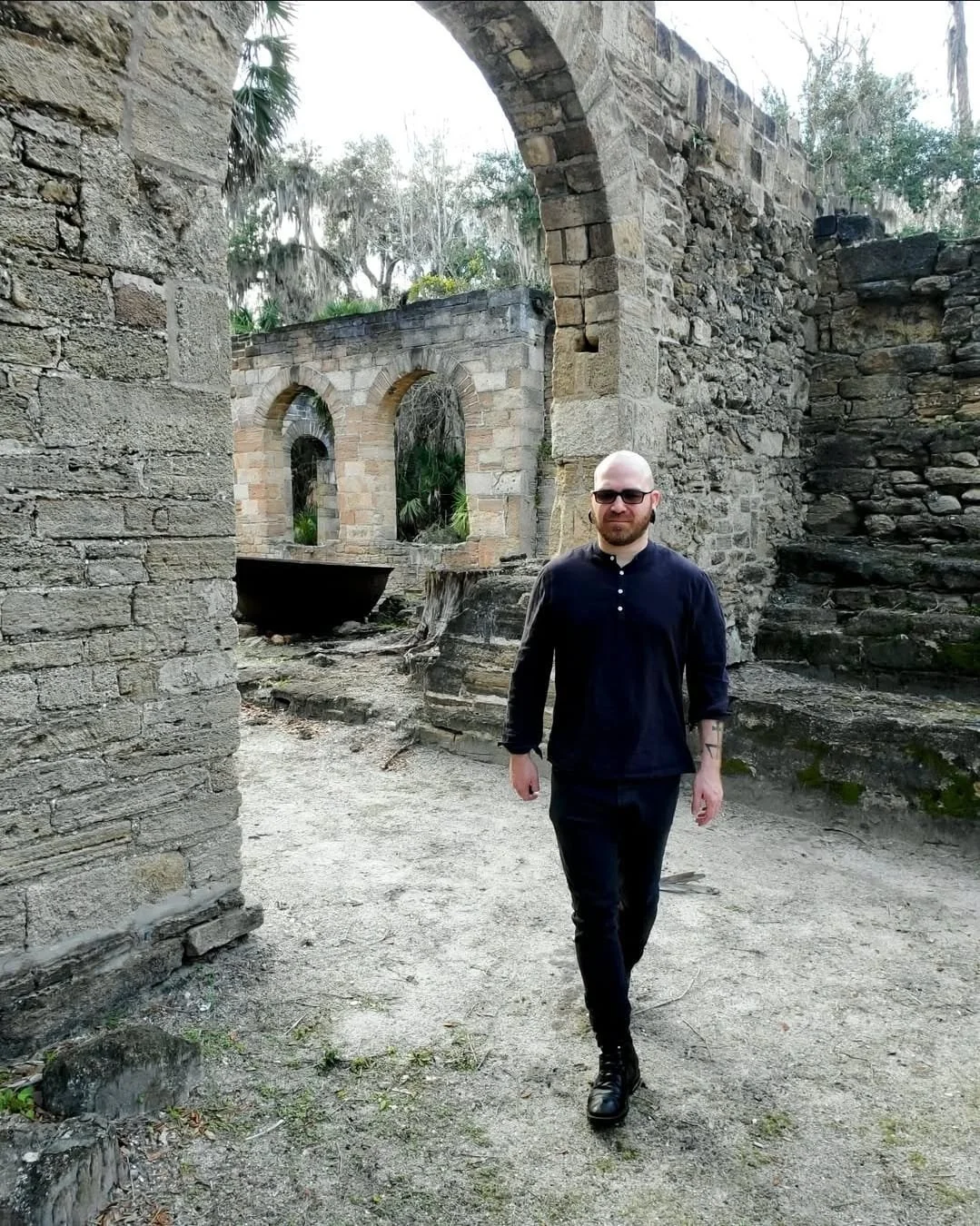 Shea Bilé is walking through ancient stone ruins with arches and stairs.