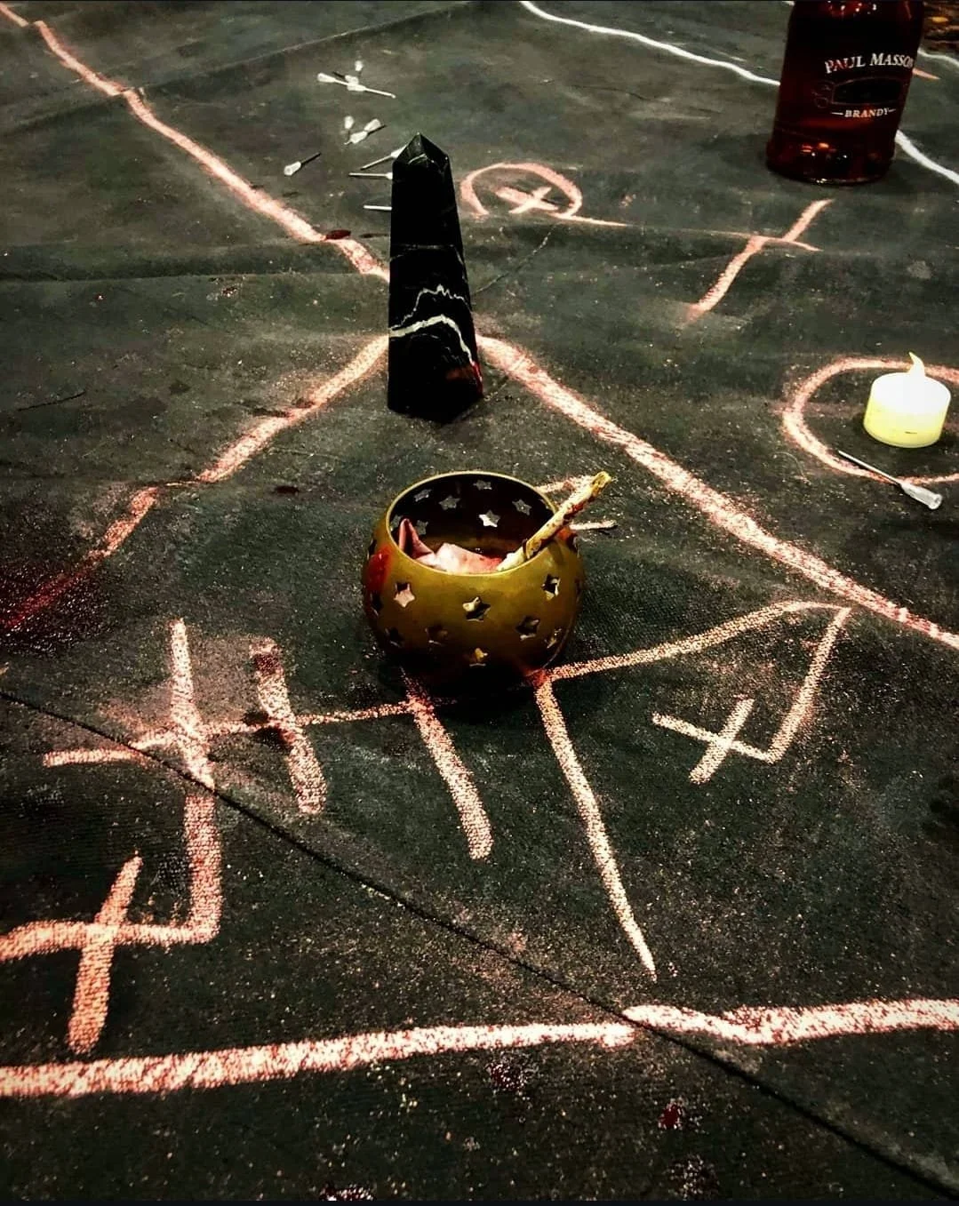 A black ritual mat contains ceremonial markings, ritual objects lie on the blood-covered mat.