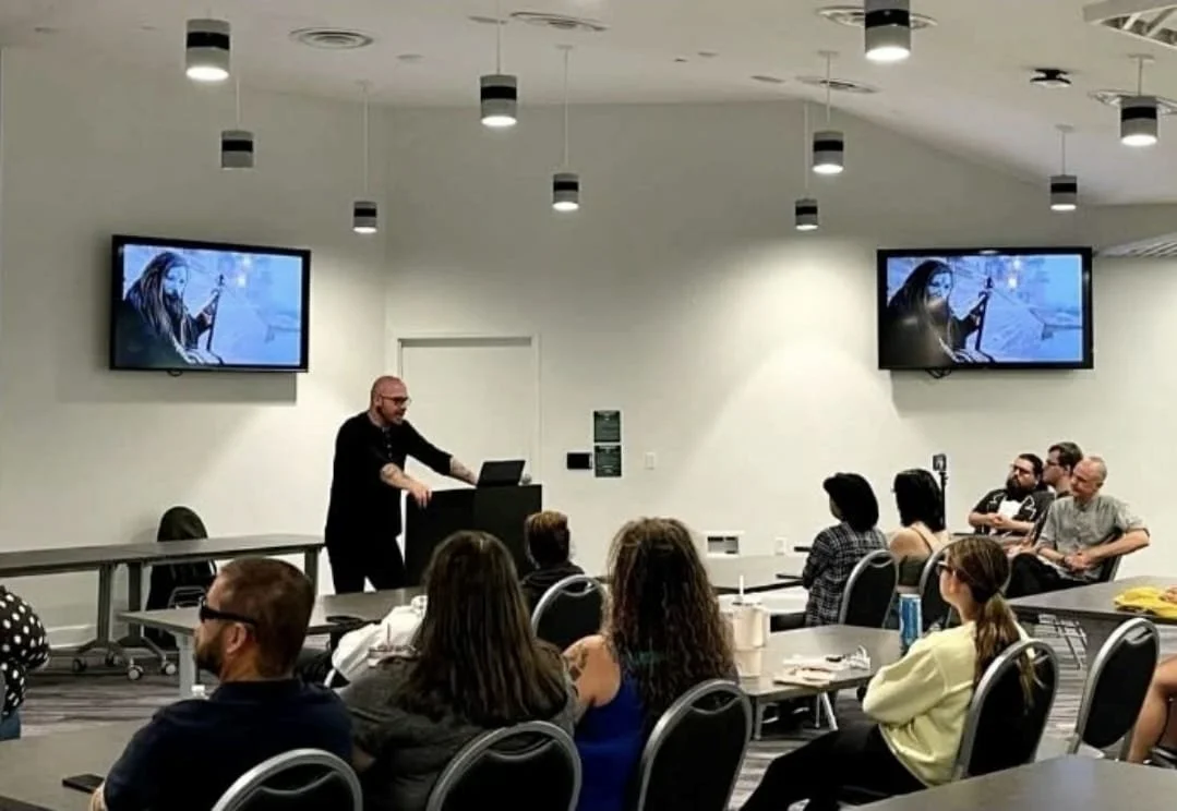 Shea Bilé gives a presentation to an audience in a conference room with two screens displaying an Aghori priest. Stetson University. Religion of Satan lecture.