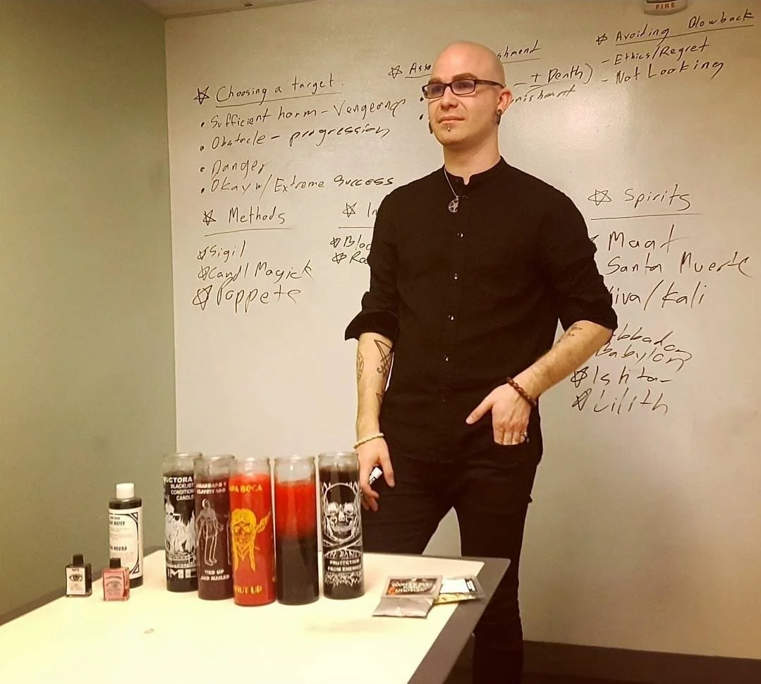 Shea Bilé stands next to a table with candles and small bottles in a room with a whiteboard filled with handwritten notes in the background.
