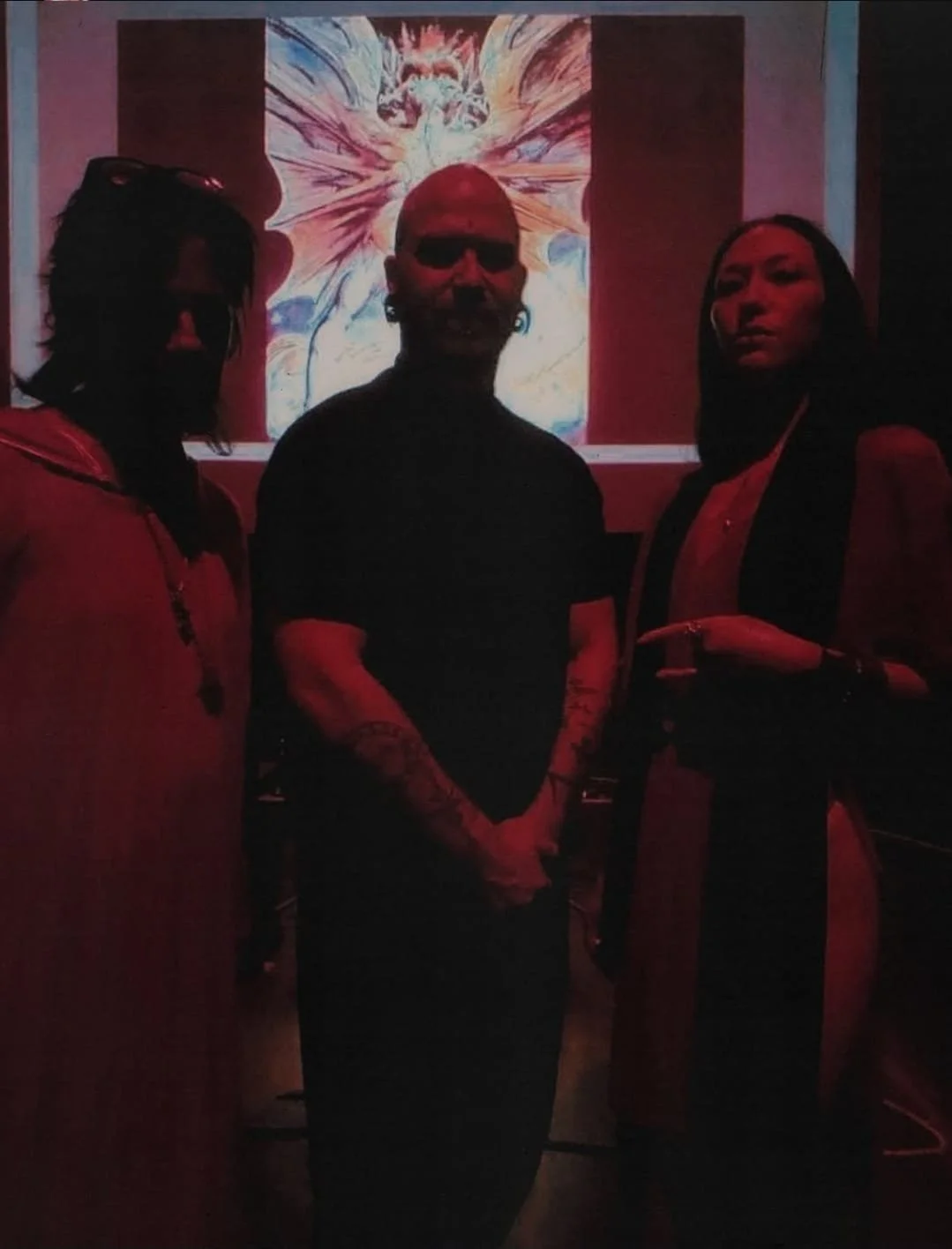 Shea Bilé, Luzia Lowe, and Sal Santoro stand in front of a large image of the Great Red Dragon by William Blake in a dimly lit room.