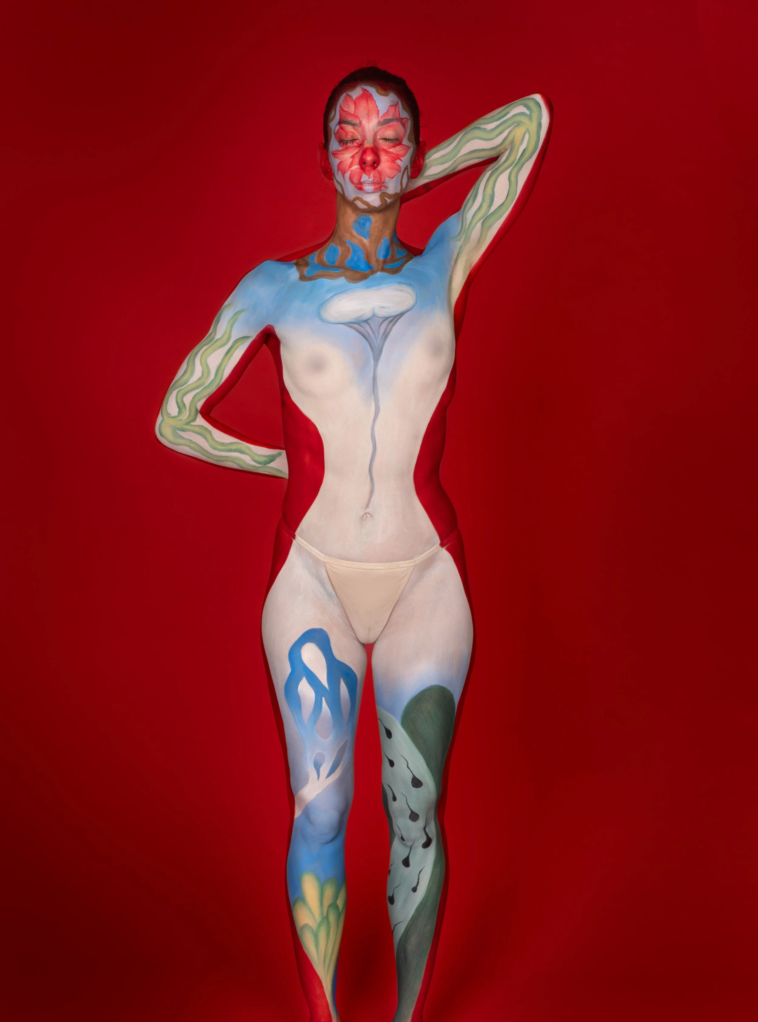 Personne avec un maquillage et un body peint à la main, posant avec les bras derrière la tête, sur un fond rouge.
