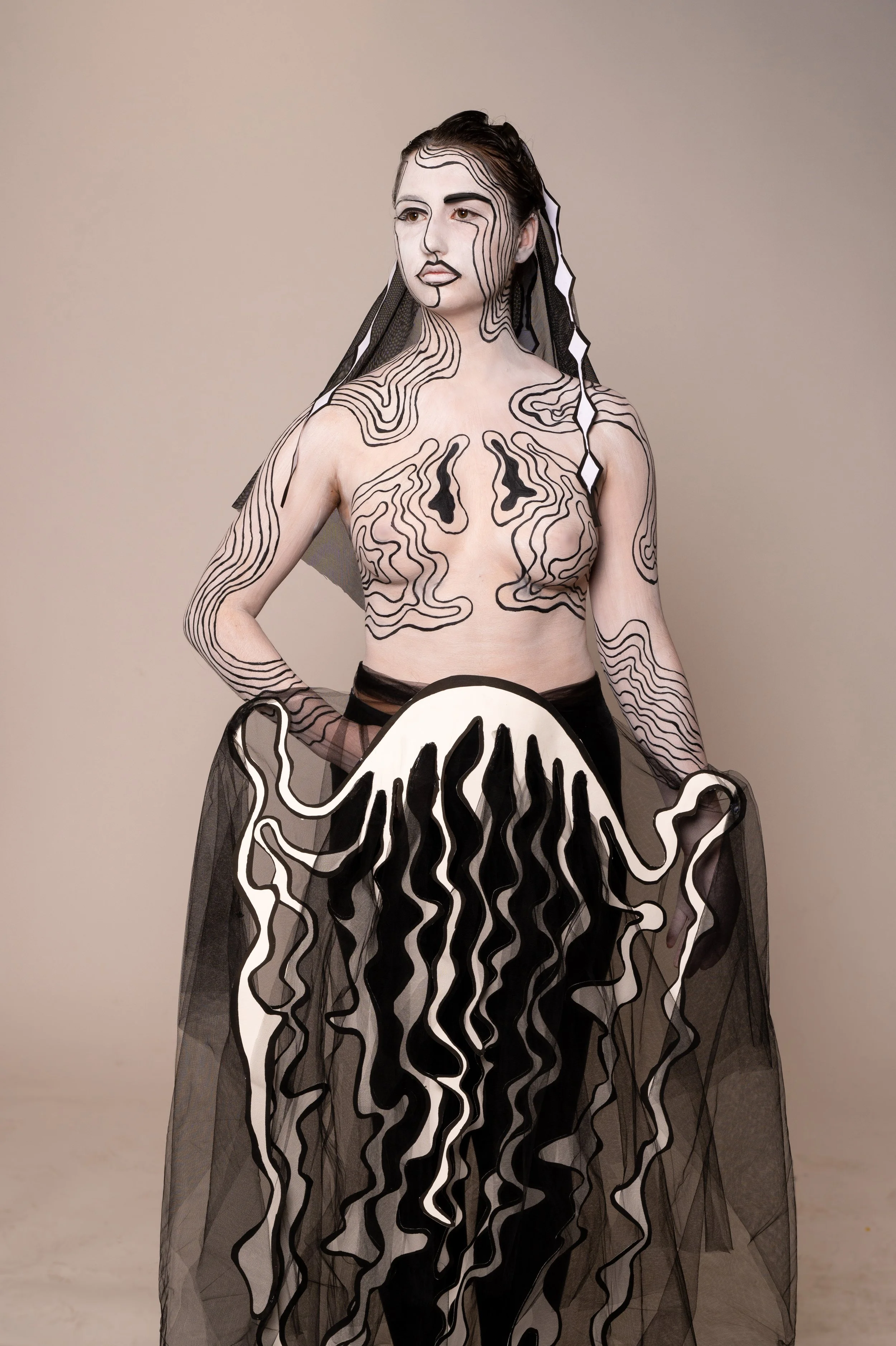 Une femme porte une tenue artistique utilisant des lignes noires et blanches, avec du tulle noir, créant un effet abstrait et moderne.