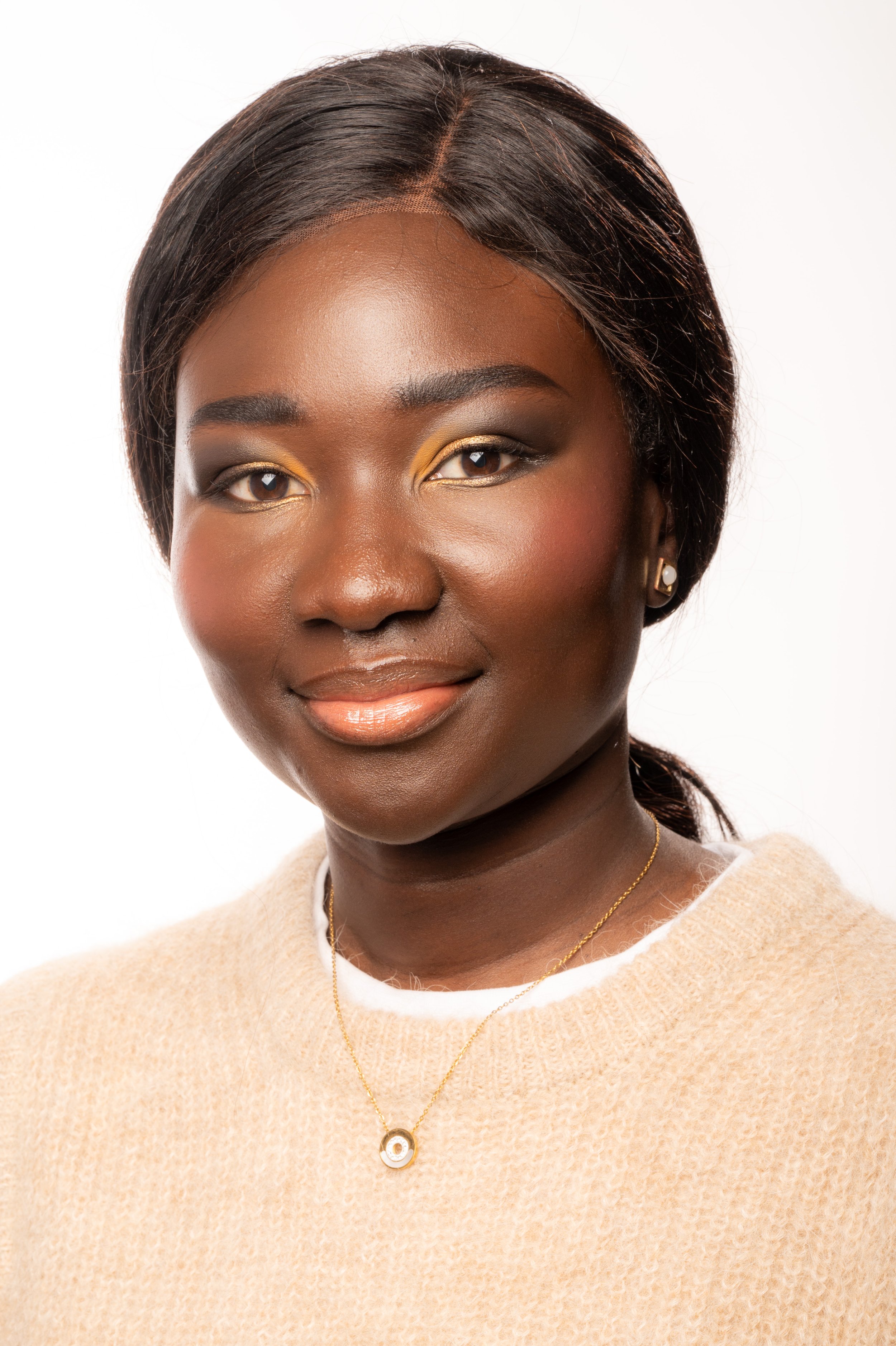 Portrait d'une femme noire avec un maquillage doré et un pull beige, portant un collier or.