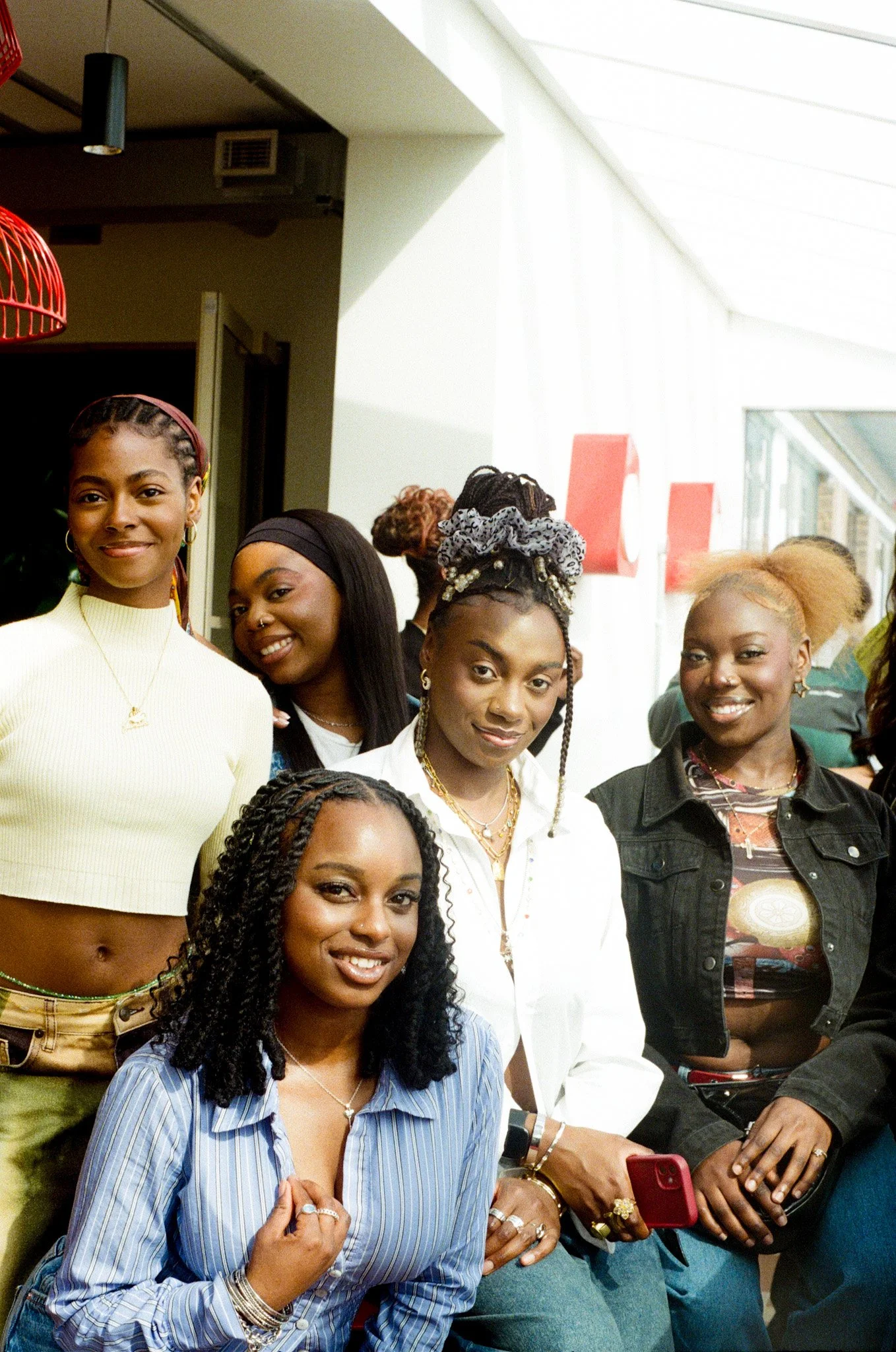 Group of diverse women smiling indoors, some holding phones.