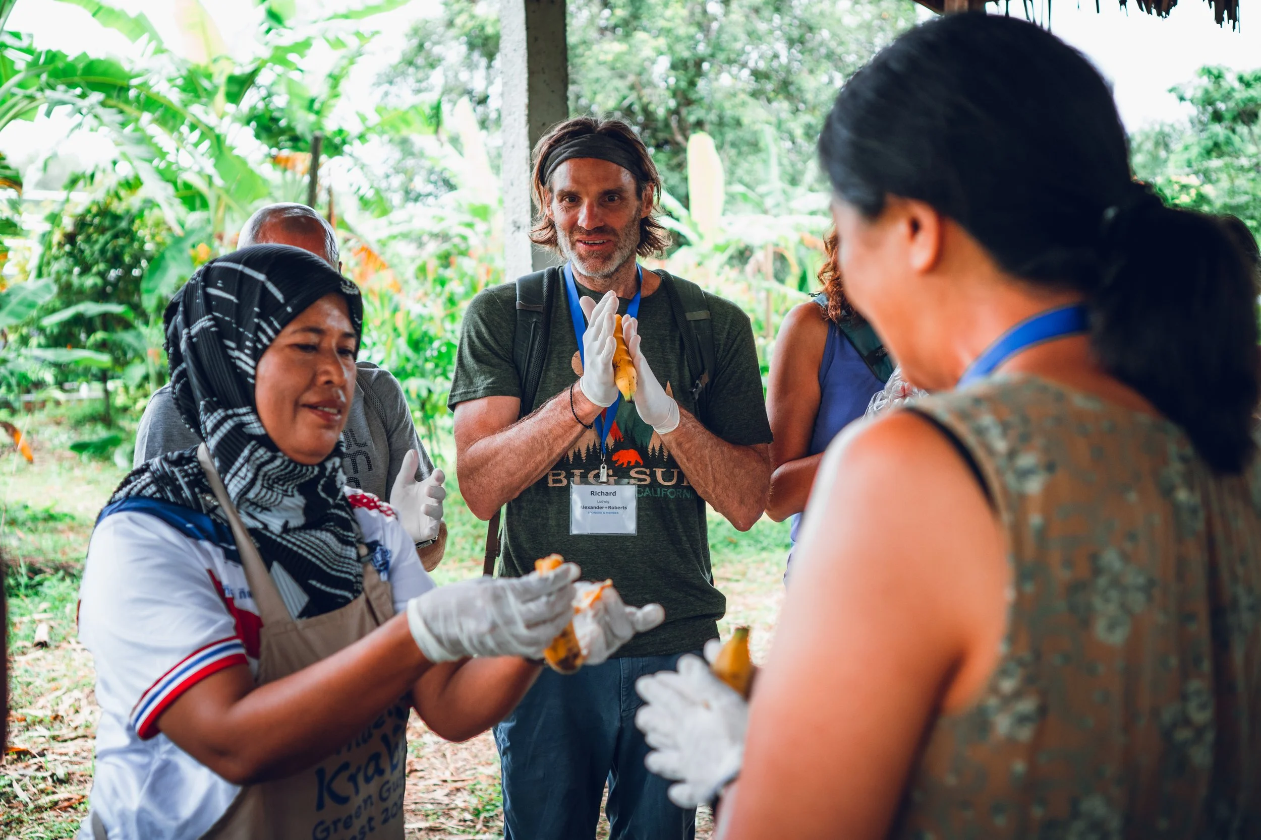 A local Thai woman wearing a headscarf and gloves prepares food for a group of tourists.
