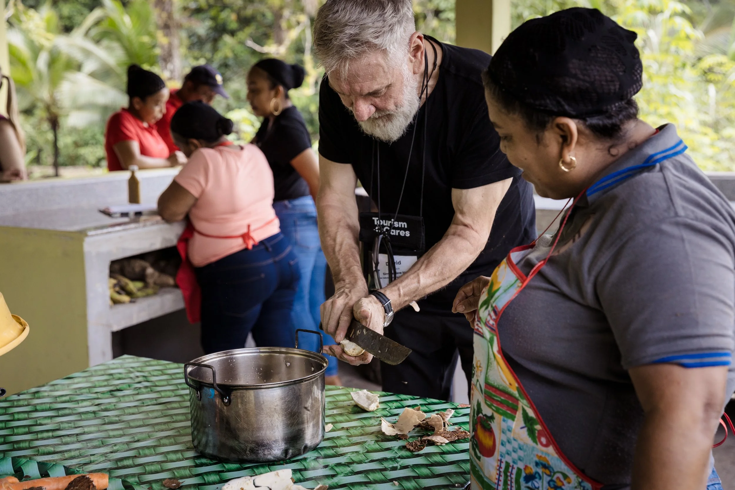 A man wearing a black shirt cuts a yucca plant alongside a woman cook in Panama