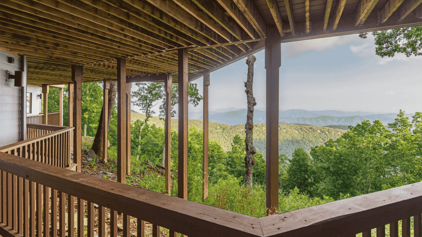 View from a wooden balcony overlooking a lush green forest and distant mountains.