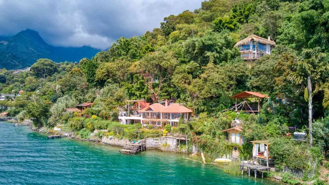 Houses on a lush hillside overlooking a blue body of water.
