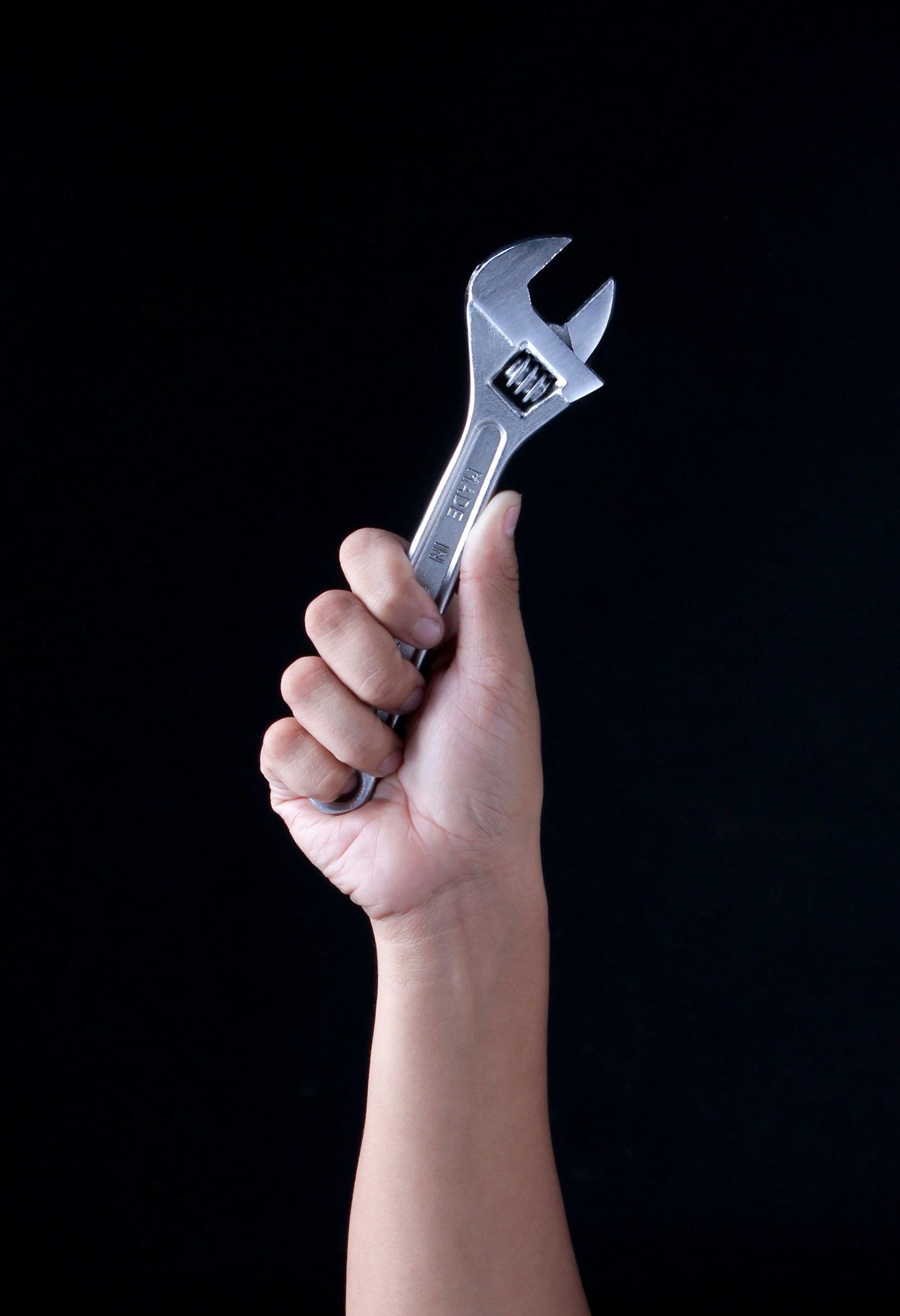 Hand holding a silver adjustable wrench against a black background.