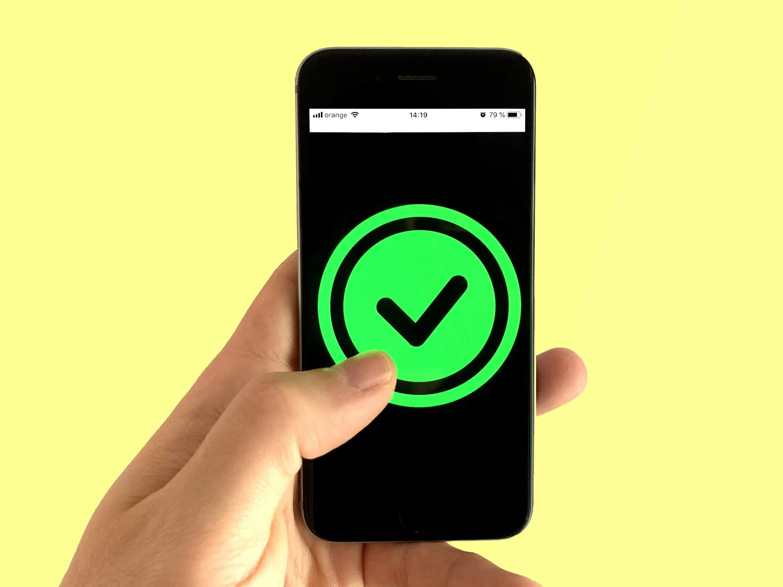 A person holding a smartphone displaying a large green checkmark symbol on the screen against a yellow background.