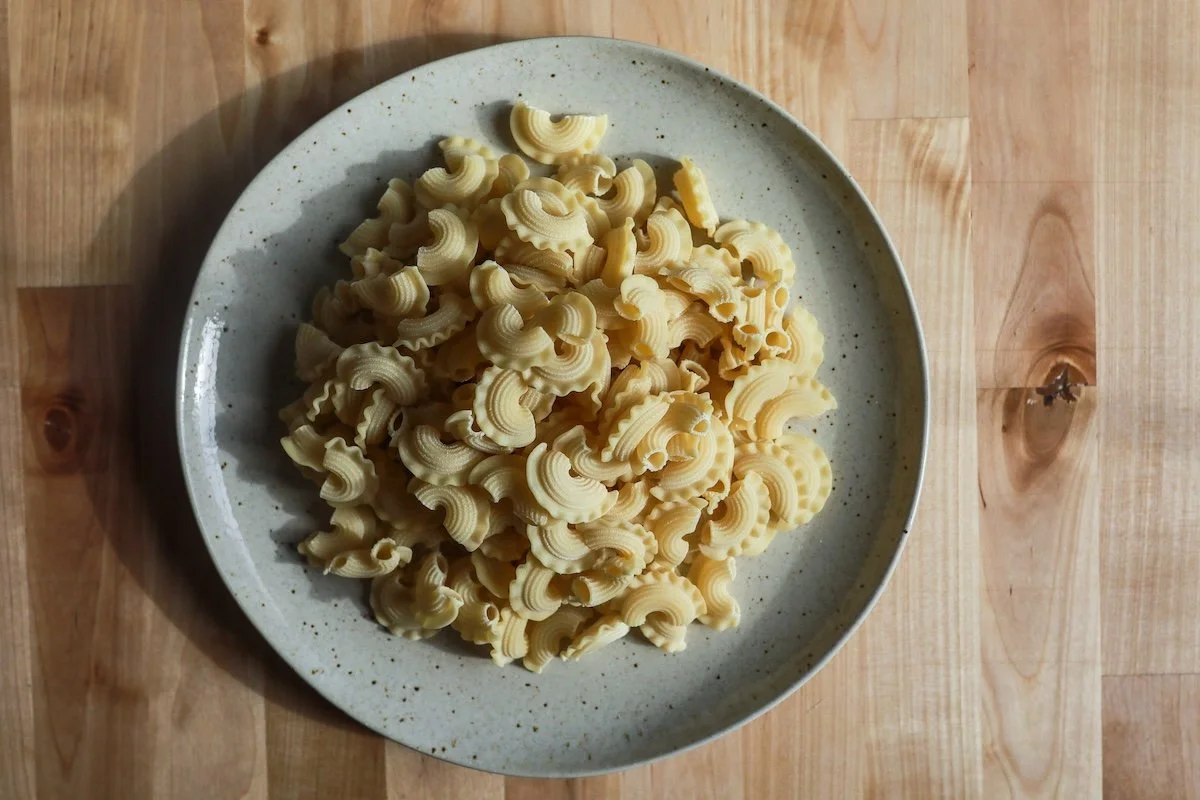 A plate of uncooked pasta shells on a wooden table.