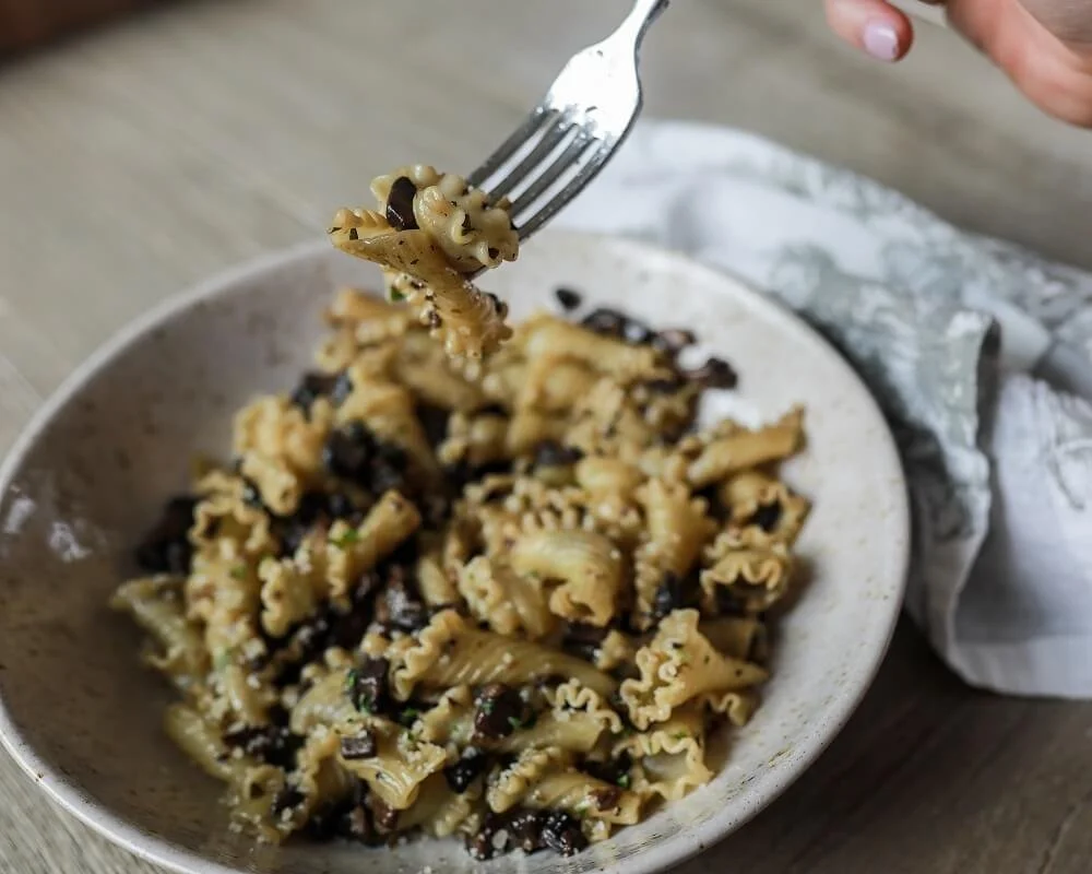 A fork with a bite of pasta lifted above a bowl of cooked bowtie pasta with black beans and chopped herbs.