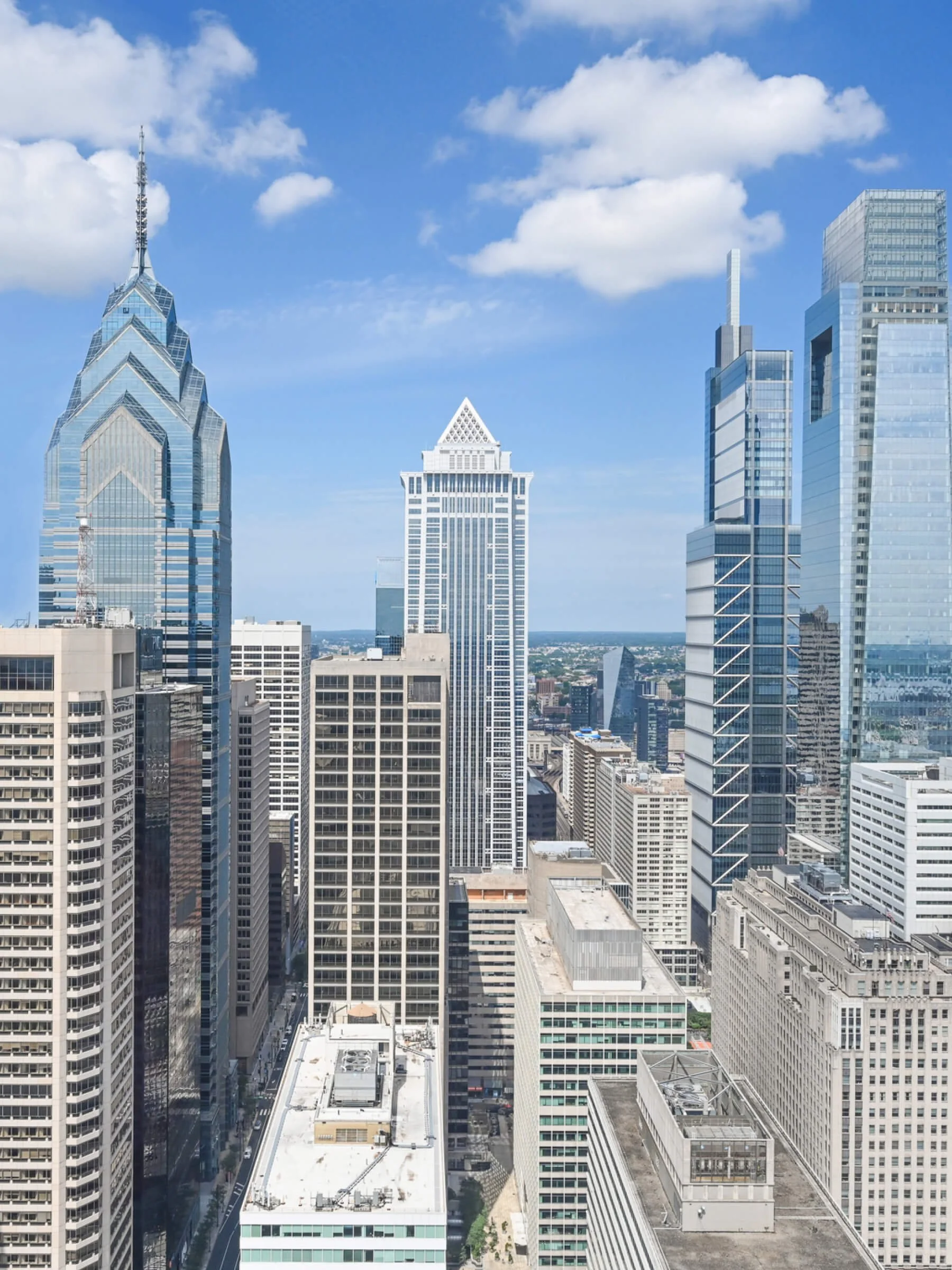 Skyline of Philadelphia with tall modern skyscrapers against a blue sky with clouds.