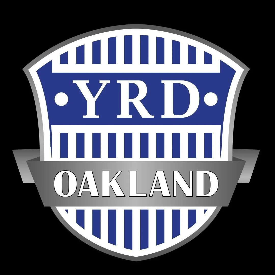 Logo of YRD Oakland with a shield shape, blue and gray colors, and striped pattern.